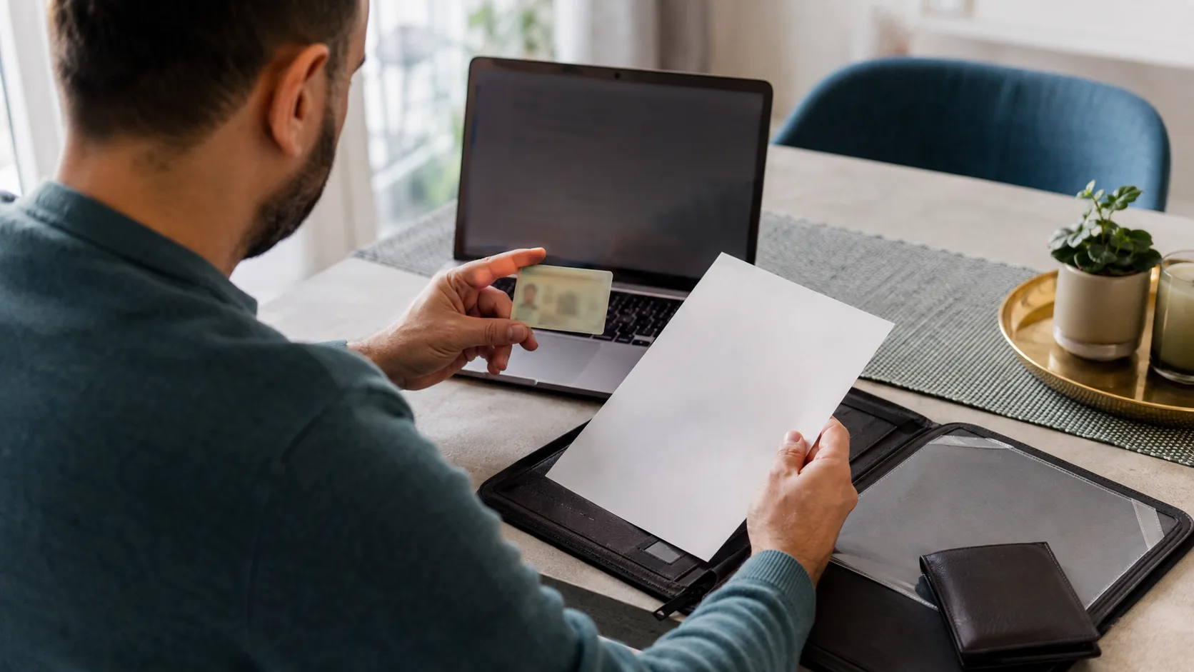 Adult organising identification paperwork beside a closed laptop in a bright home office